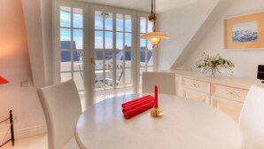 Un coin repas avec une table ronde, des chaises blanches, une bougie rouge et une suspension.