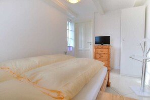 A bedroom with a bed, a television on a dresser, and a door. - Holiday apartment in Sylt with 1 bedroom (Wenningstedt)