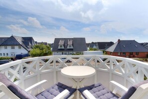 A balcony with a round table and two cushioned chairs, overlooking a residential area with houses and a clear sky. - Holiday apartment in Sylt with 1 bedroom (Wenningstedt)