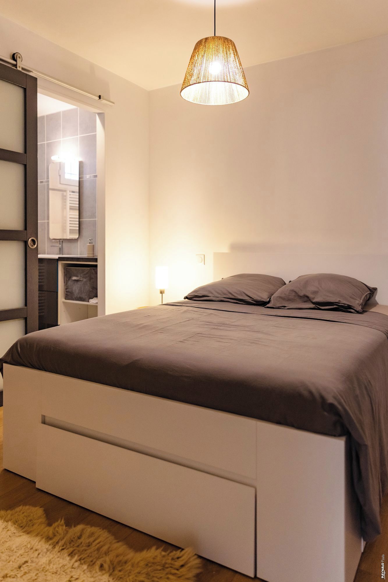 Een slaapkamer met een bed, een hanglamp, een spiegel en een kledingkast.