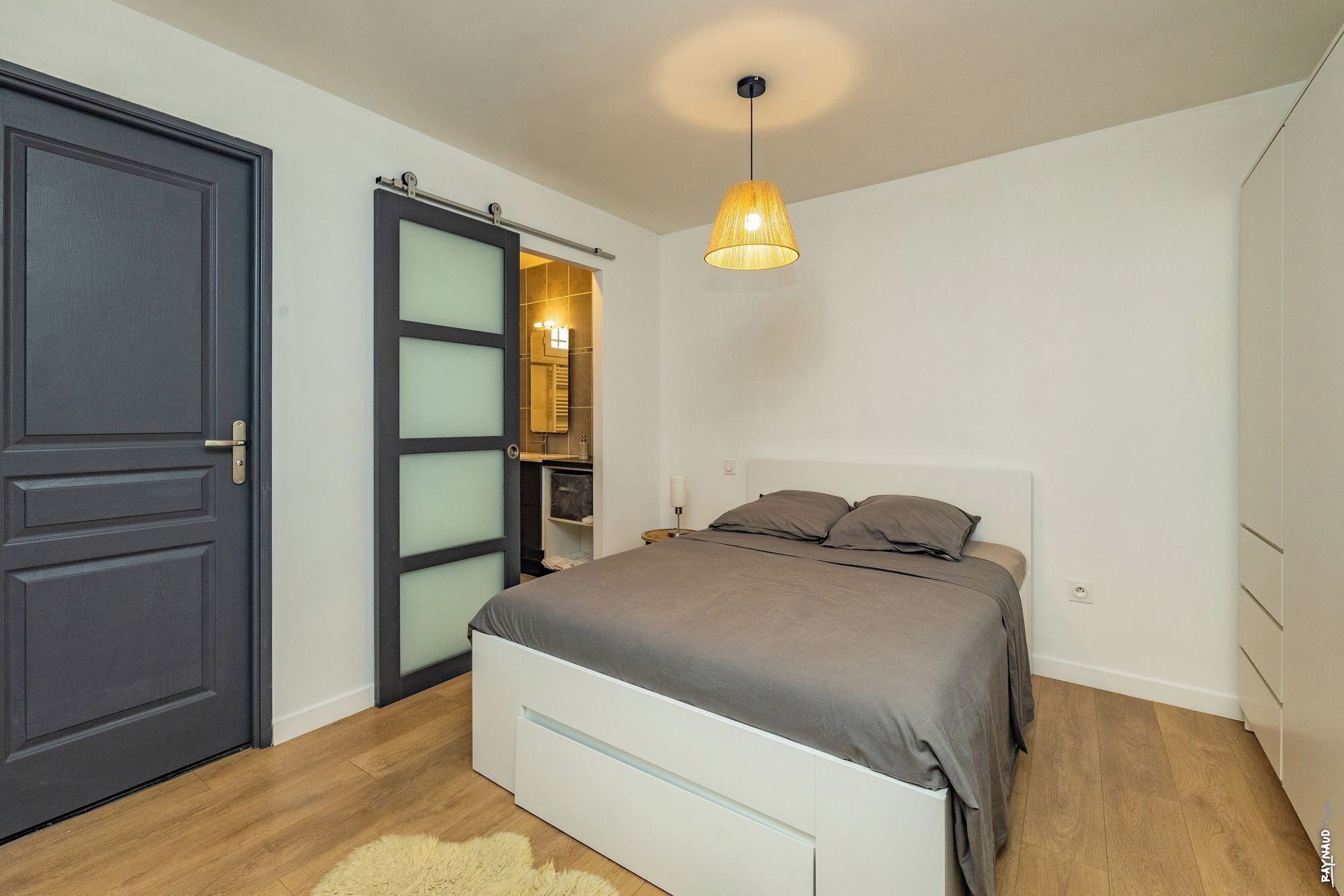 A bedroom with a bed, a door, and a hanging light fixture.