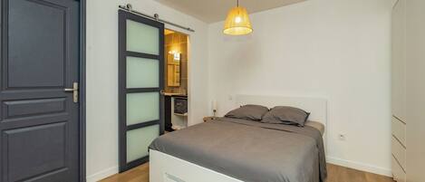 Un dormitorio con cama, una puerta y una lámpara colgante.