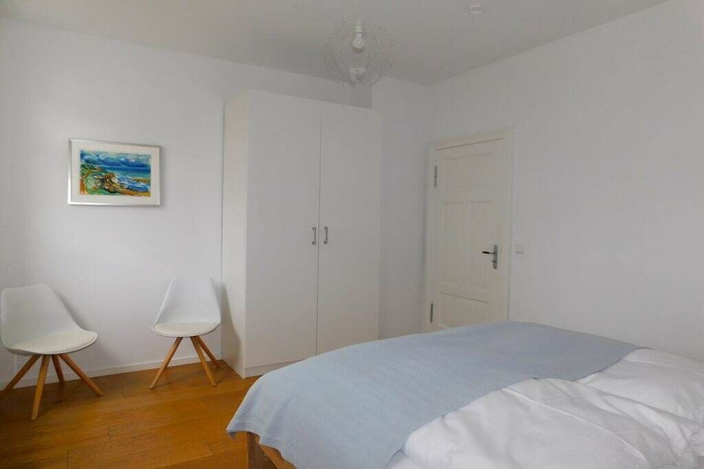 Une chambre à coucher avec un lit, deux chaises, une armoire et un tableau au mur.