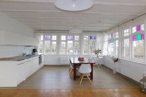 A spacious kitchen with a dining area, large windows with colorful panes, and a modern light fixture. - Holiday apartment with 1 bedroom (Ostseebad Ahrenshoop)