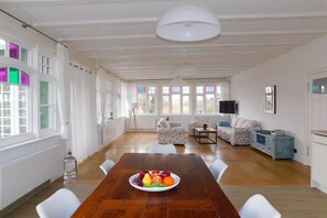A spacious room with a wooden dining table, white chairs, a sofa, and a television. - Holiday apartment with 1 bedroom (Ostseebad Ahrenshoop)