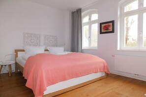 Et soveværelse med seng, et natbord, et vindue med gardiner og en radiator.