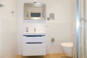Et badeværelse med et hvidt håndvask, spejl og toilet.