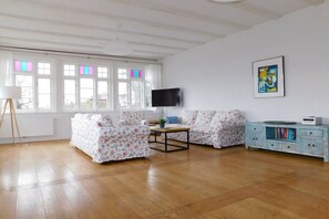 A living room with two floral sofas, a coffee table, a TV on the wall, and a bookshelf. - Holiday apartment with 1 bedroom (Ostseebad Ahrenshoop)