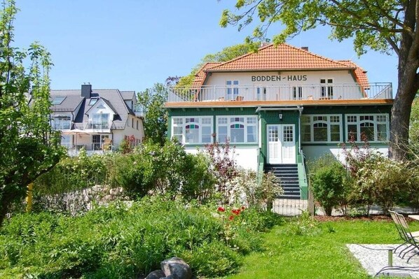 En toetagers bygning, Bodden-Haus, med balkon, omgivet af grønt og en have.