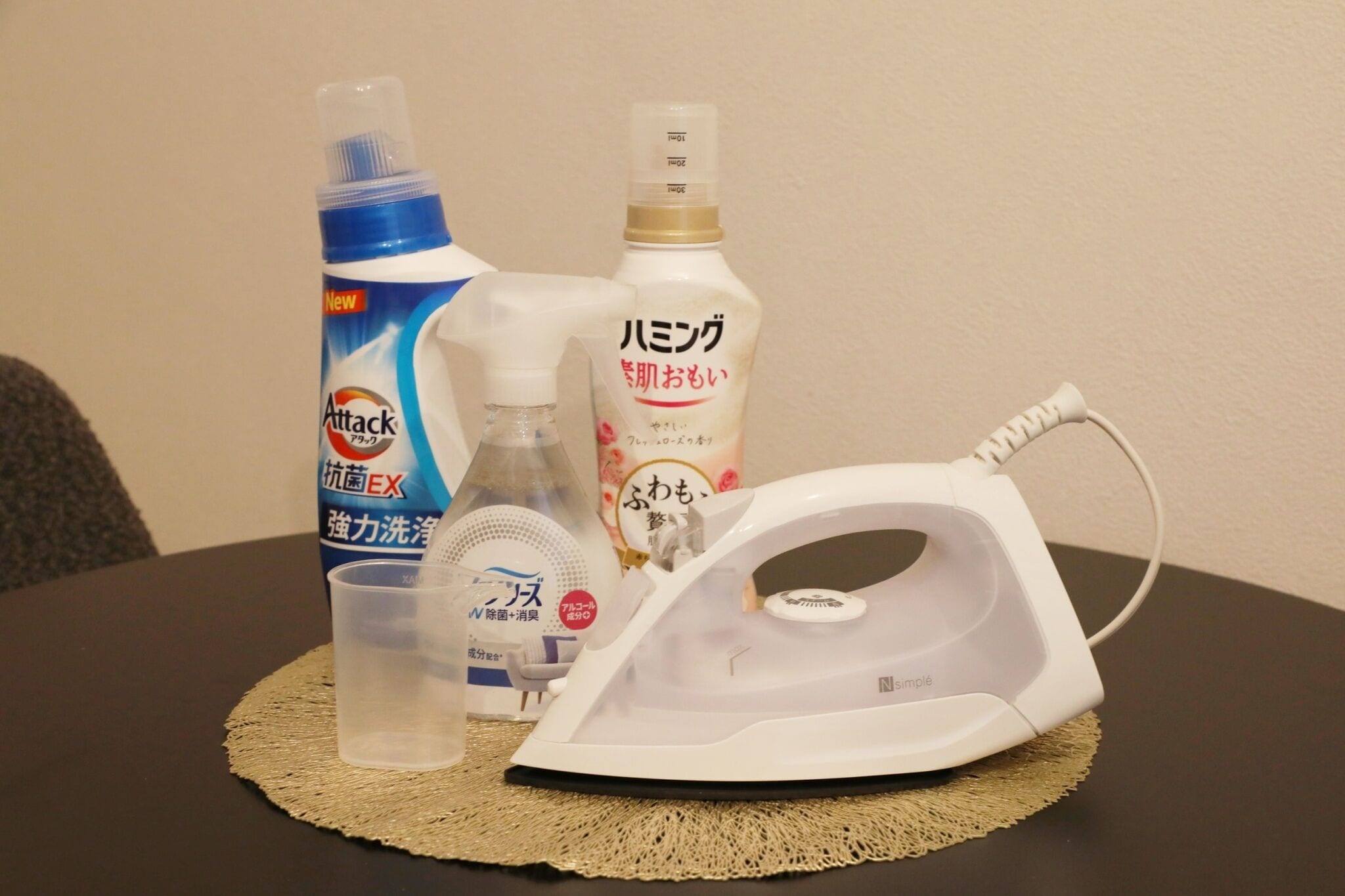 Una mesa con un hierro para planchar, una botella de líquido, un pulverizador y una caja de detergente.