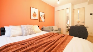 A hotel room with a bed, a sofa, a chair, and a desk. There are two framed pictures on the wall. - Sakura Court Ebisu (Shibuya)