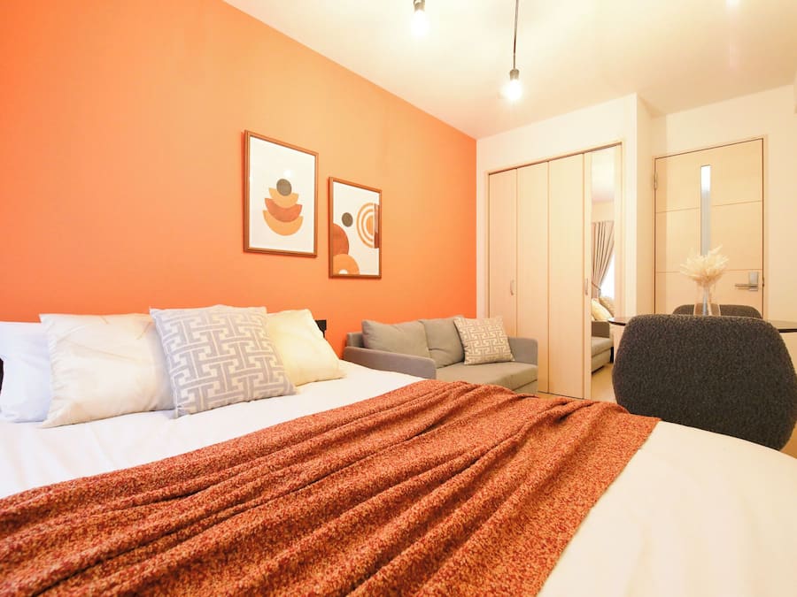 Habitación de hotel con cama, sofá, sillón y escritorio. Dos cuadros decoran la pared.