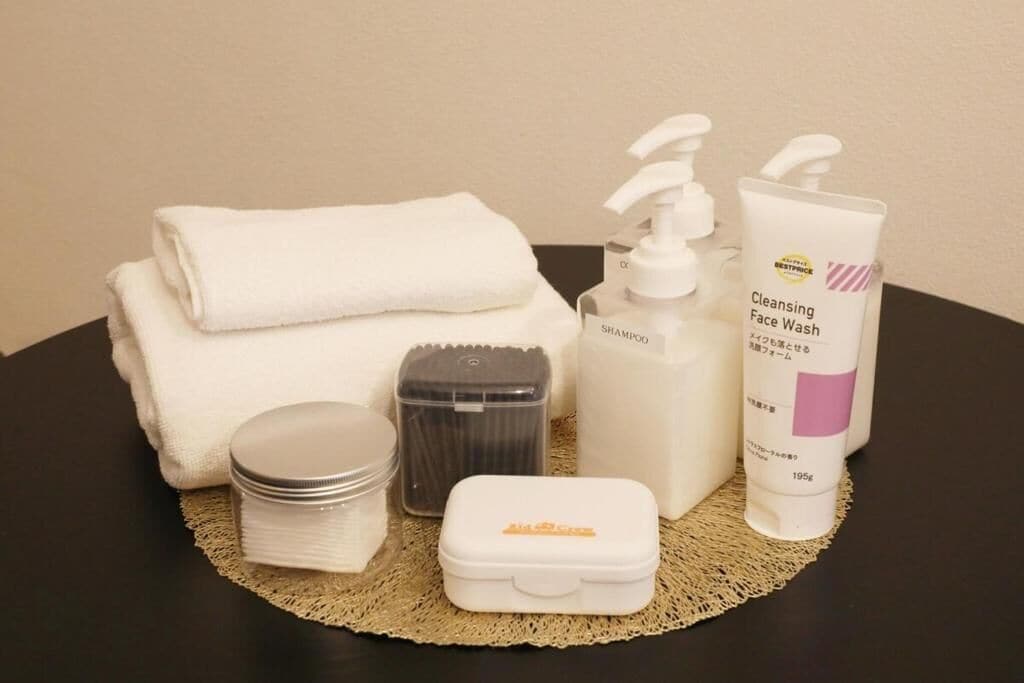 A neatly arranged bathroom with a towel, shampoo, face wash, and other toiletries on a table.