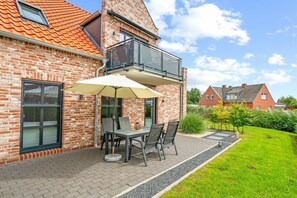 Une maison en briques avec un balcon, une terrasse avec une table et des chaises, et un jardin bien entretenu.