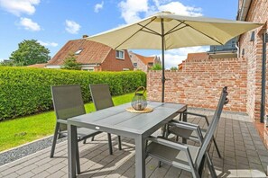 Une terrasse extérieure avec une table et des chaises, un grand parasol et un mur en briques.