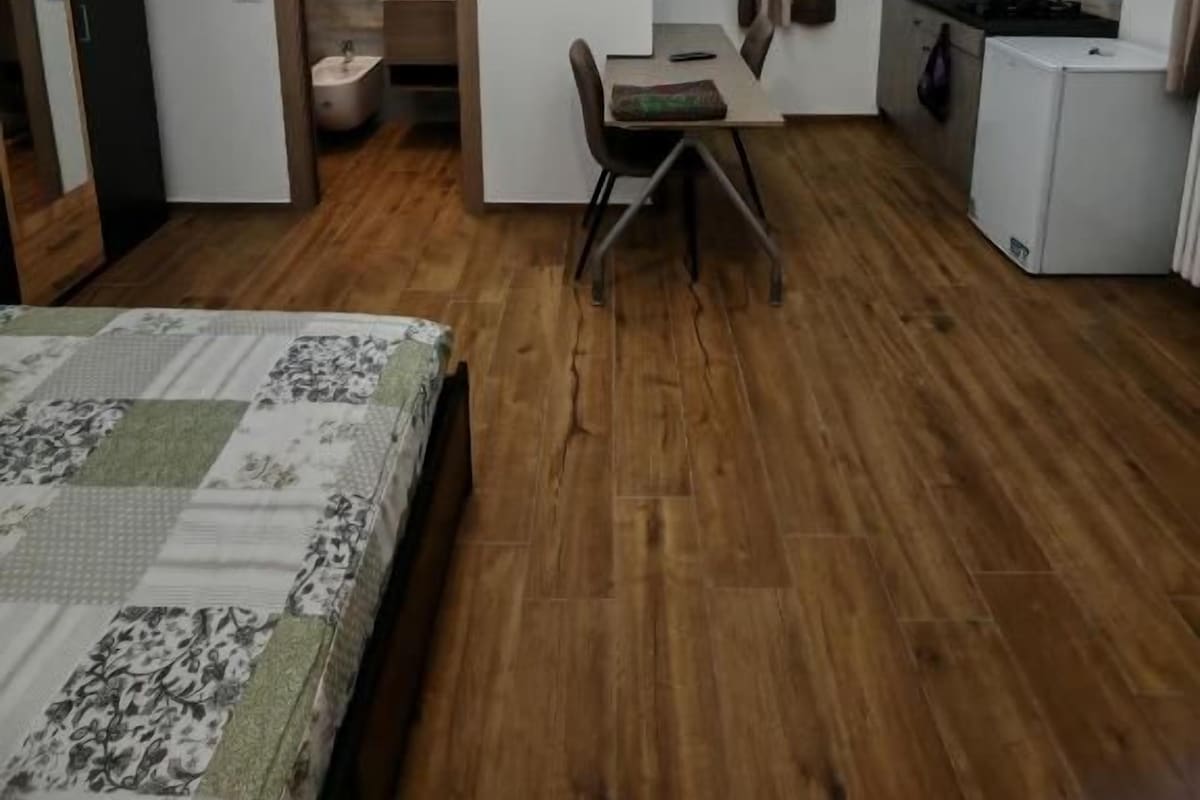 A compact room with a bed, a desk, a chair, a small kitchenette, and a window with curtains.