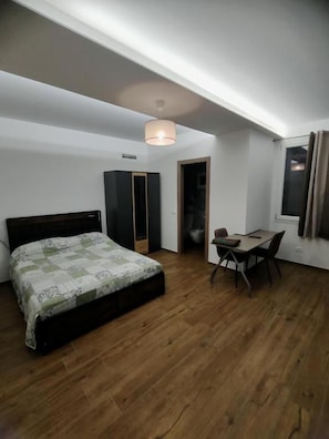 A bedroom with a bed, a desk, and a chair. There is a window with curtains, a door, and a ceiling light fixture. - B&B RioReno (CITTÀ METROPOLITANA DI BOLOGNA)