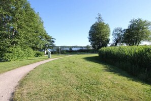 Ein grasbewachsener Pfad führt zu einem weißen Gebäude mit freiem Blick auf ein Gewässer in der Ferne.