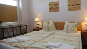 A bedroom with a large bed, two bedside tables with lamps, a window with blinds, and artwork on the walls. - 14 in the Quisisana house (Westerland)