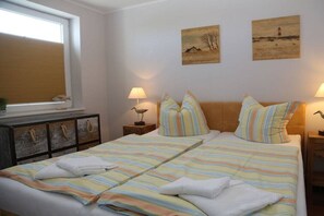 Ein Schlafzimmer mit einem großen Bett, zwei Nachttischen inklusive Lampen, einem Fenster mit Jalousien und Bildern an den Wänden.