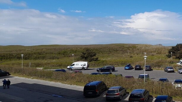 A parking lot with several cars and a white van, surrounded by grassy fields and a clear sky. - 14 in the Quisisana house (Westerland)