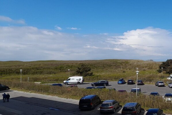 Ein Parkplatz mit mehreren Autos und einem weißen Lieferwagen, umgeben von grünen Wiesen und einem klaren Himmel.