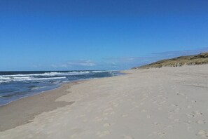 A wide sandy beach with footprints leading to the water, a clear sky, and distant hills. - 14 in the Quisisana house (Westerland)
