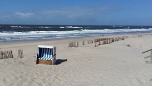 A beach with a single striped beach chair and a wooden structure, possibly a lifeguard station, with the ocean in the background. - 14 in the Quisisana house (Westerland)