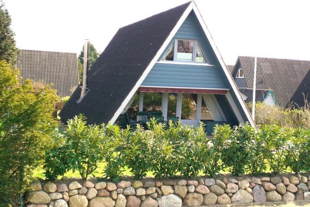 Una casa amb un teulat triangular, un mur de pedra al primer pla i una tanca de fusta de fons.