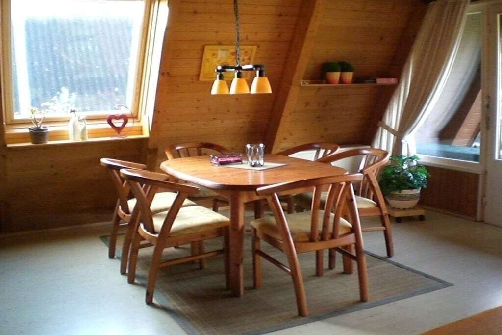 A wooden dining table with six chairs, a hanging light fixture, and a window with a view.
