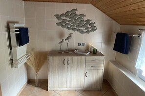 Ein Badezimmer mit Holzboden, einer hell gefliesten Wand, einem Holzkabinent mit Schubladen und einem Handtuchhalter.