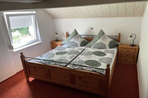 Ein Schlafzimmer mit einem hölzernen Bett, gemusterten Betttextilien, Nachttischen und einem Fenster mit Jalousien.