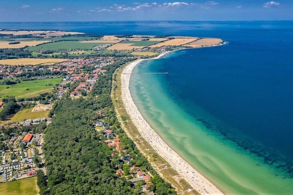 An aerial view of a coastal town with a long sandy beach, a clear blue sea, and surrounding green fields.