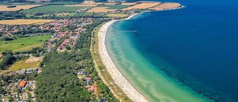 An aerial view of a coastal town with a long sandy beach, a clear blue sea, and surrounding green fields.