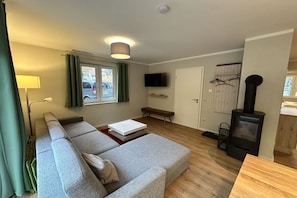 A modern living room with a sofa, a television, a bench, and a wood-burning stove. - Beach house Seeperle Apt. Seerose (Ostsee Bad Boltenhagen)