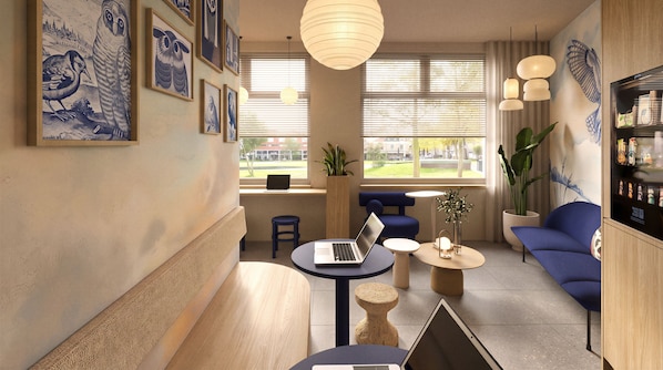 Un área de descanso moderna con una laptop sobre una mesa, una planta en maceta y una zona de estar con sofás azules.