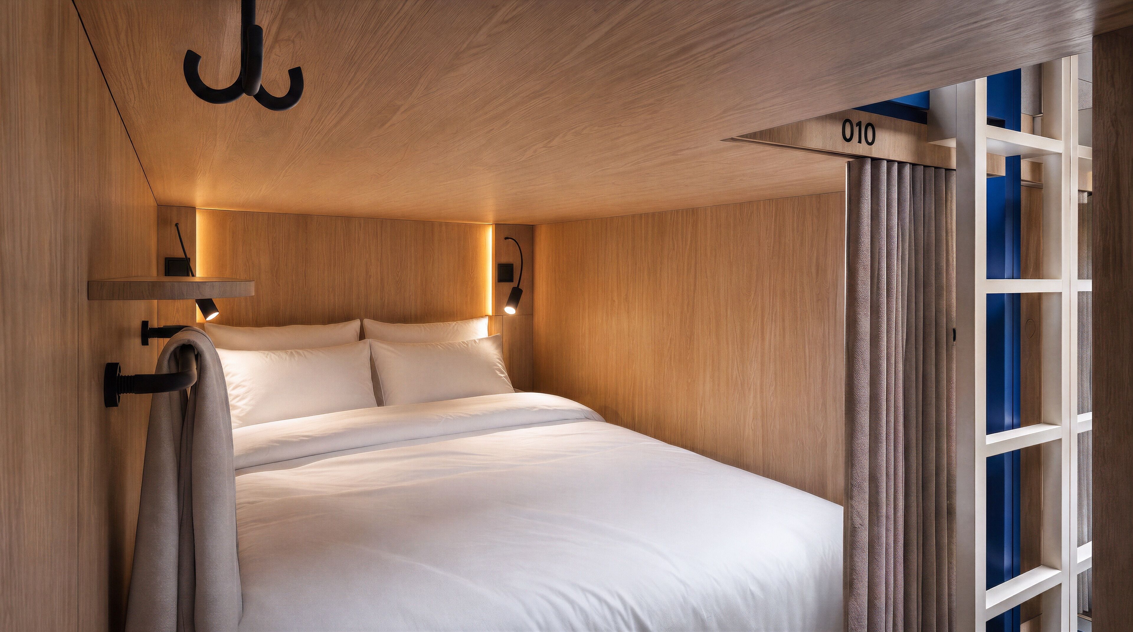 Une chambre moderne avec une tête de lit en bois, un lit avec une literie blanche et une étagère intégrée portant le numéro 010.