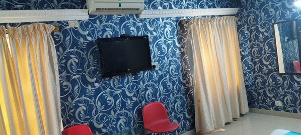 Una habitación con papel tapiz estampado, un televisor montado y dos sillas rojas.