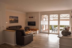A modern living room with a sofa, a flat-screen TV, and a dining area with a table and chairs. - Holiday apartment with 2 bedrooms (Norden)