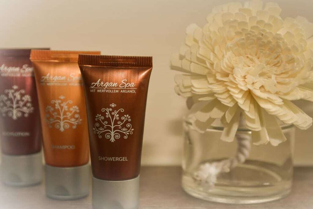Three bottles of Argan Spa shower gel next to a vase with a white flower.