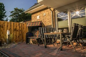An outdoor patio with a brick floor, a wooden fence, and a covered seating area with striped cushions. - Holiday apartment with 2 bedrooms (Norden)