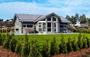 A modern two-story house with a large deck, a stone wall, and a well-maintained lawn.