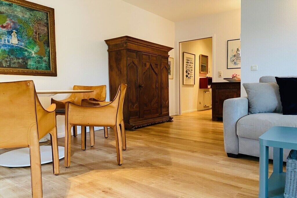 Un coin repas avec des chaises et une table en bois, une grande armoire en bois, un canapé gris et un tableau encadré accroché au mur.
