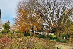 Ein Wohngebiet mit Häusern, einem großen Baum mit Herbstlaub und einem gepflegten Garten.