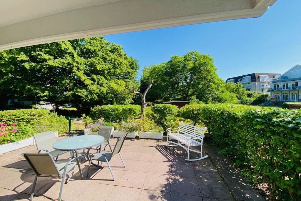 An outdoor patio with a table and chairs, surrounded by greenery and a clear sky.