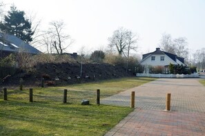 Een verhard pad leidt naar een huis met schuin dak, omringd door gazon en bomen.