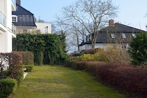 A residential area with a well-maintained lawn, hedges, and a pathway leading to a house with a dark roof. - Apartment in Travemünde with swimming pool (Travemünde)