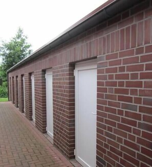 Une rangée de bâtiments en briques avec des portes blanches, probablement un espace de stockage ou un local technique.