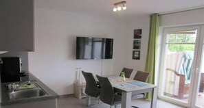 Une cuisine compacte équipée d’un téléviseur à écran plat, d’une table à manger avec des chaises et d’une porte-fenêtre coulissante donnant sur un espace extérieur.