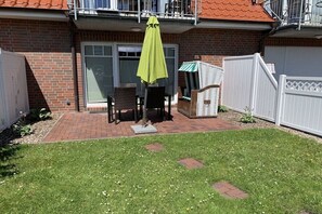 A patio with a table and chairs, a green umbrella, and a white fence. - Holiday apartment with 1 bedroom (Norddeich)